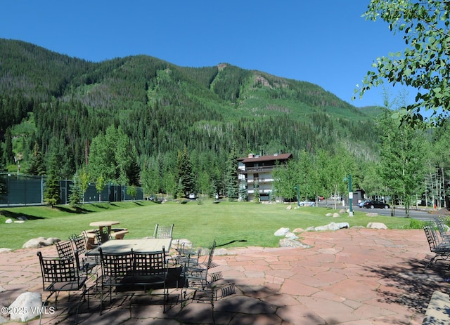 view of property's community with a patio area, a lawn, a mountain view, and a view of trees