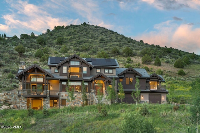 420 Little Andorra Rd, Edwards, CO 81632 - view of front of property featuring a balcony, roof mounted solar panels, stone siding, an attached garage, and a chimney