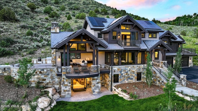 420 Little Andorra Rd, Edwards, CO 81632 - back of property at dusk with a balcony, stone siding, solar panels, a patio area, and stucco siding