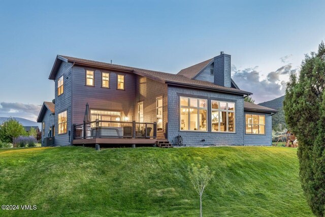 rear view of property with a wooden deck, a lawn, and cooling unit