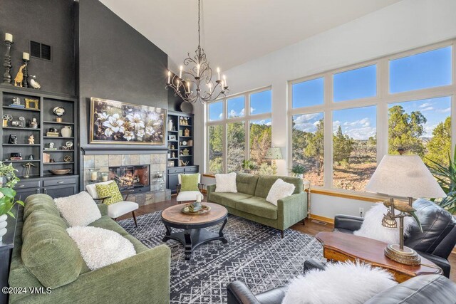 living room featuring high vaulted ceiling, a chandelier, hardwood / wood-style flooring, a tiled fireplace, and built in shelves