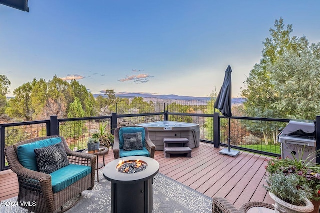 deck at dusk with an outdoor fire pit, a hot tub, a mountain view, and a grill