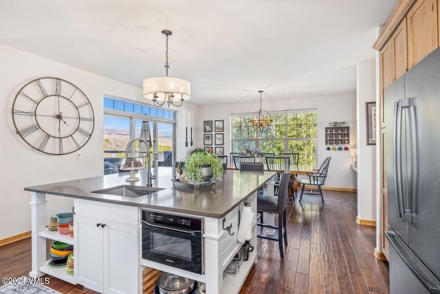 kitchen featuring stainless steel refrigerator, white cabinetry, sink, a center island with sink, and an inviting chandelier