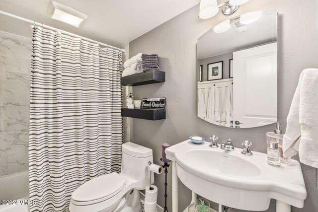 full bathroom featuring sink, shower / bath combo with shower curtain, and toilet