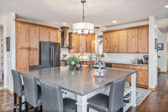 kitchen featuring pendant lighting, wall chimney range hood, sink, fridge, and an island with sink