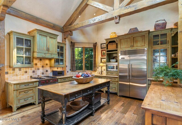 kitchen with beamed ceiling, green cabinetry, built in appliances, hardwood / wood-style flooring, and backsplash