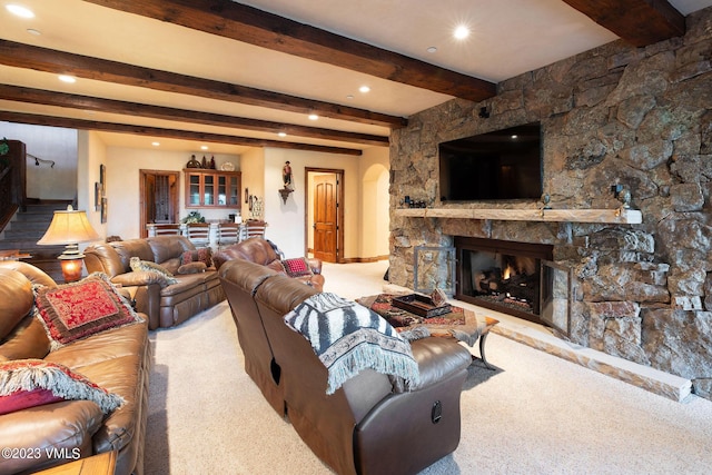 living room with beamed ceiling, carpet, and a stone fireplace