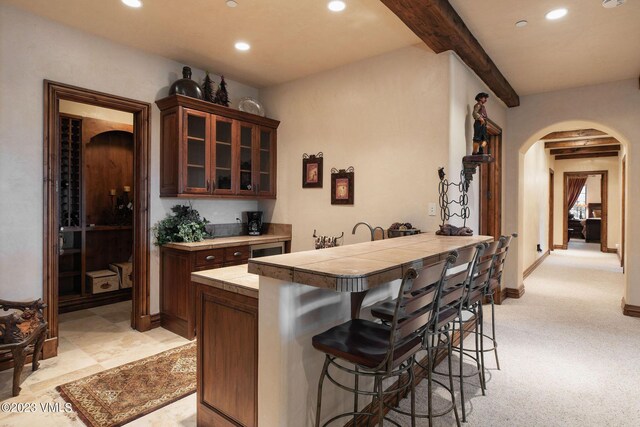 bar with dark brown cabinetry, tile countertops, light carpet, and beam ceiling