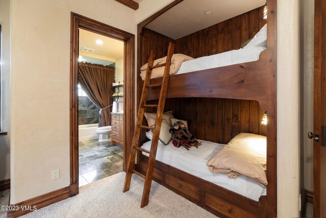 bedroom with carpet, connected bathroom, and wooden walls