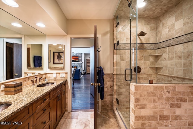 bathroom featuring a large fireplace, double vanity, recessed lighting, a stall shower, and a sink