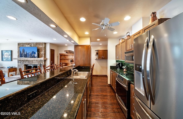 kitchen with a sink, open floor plan, appliances with stainless steel finishes, brown cabinetry, and dark wood-style flooring