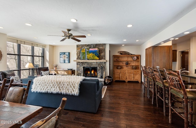 living area featuring a stone fireplace, recessed lighting, dark wood-type flooring, and ceiling fan