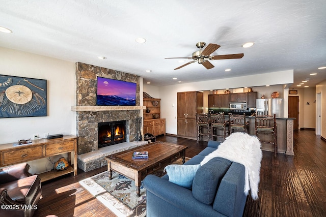 living area featuring recessed lighting, a stone fireplace, dark wood-style floors, and a ceiling fan