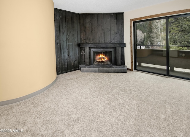 unfurnished living room featuring wooden walls, a large fireplace, carpet flooring, and baseboards