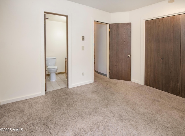 unfurnished bedroom featuring connected bathroom, a closet, baseboards, tile patterned flooring, and carpet floors