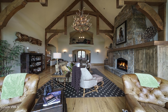 living room with a chandelier, arched walkways, a stone fireplace, and wood finished floors