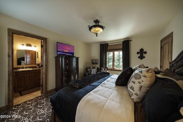 bedroom with light tile patterned floors, ensuite bath, a sink, and baseboards