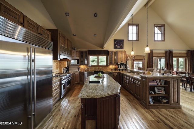 kitchen with a peninsula, premium appliances, hardwood / wood-style flooring, and light stone countertops