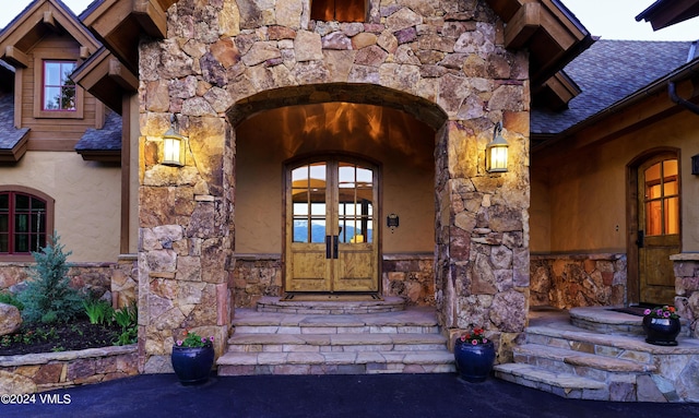 doorway to property featuring stone siding, french doors, roof with shingles, and stucco siding