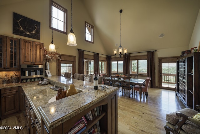 kitchen with a notable chandelier, hanging light fixtures, light wood-style floors, glass insert cabinets, and stainless steel oven