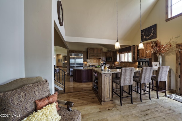 kitchen with built in appliances, arched walkways, a breakfast bar area, light wood-style flooring, and plenty of natural light