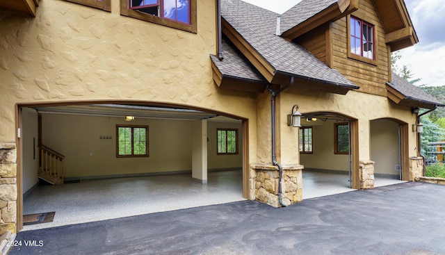 rear view of house with aphalt driveway, stone siding, roof with shingles, and stucco siding