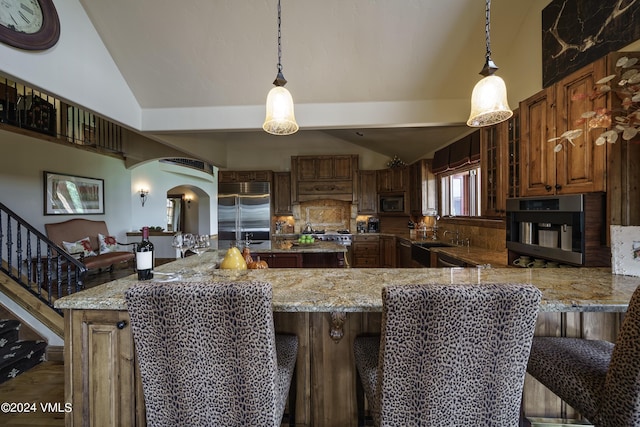 kitchen with arched walkways, vaulted ceiling, light stone counters, and built in appliances