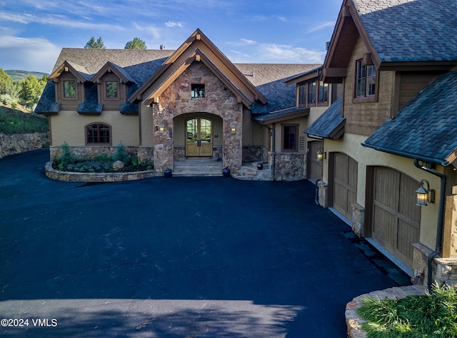 french country home with aphalt driveway, stone siding, french doors, and a garage