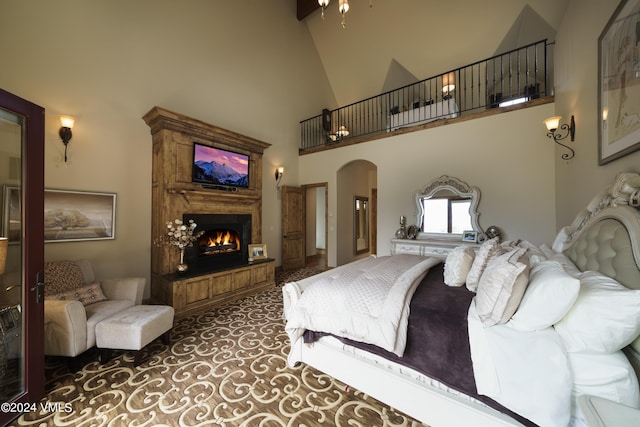 bedroom featuring a warm lit fireplace, carpet, a high ceiling, and arched walkways