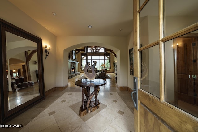 entrance foyer featuring arched walkways, a warm lit fireplace, light tile patterned flooring, and baseboards