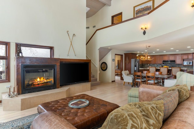 living room featuring a tiled fireplace, recessed lighting, light wood-style floors, a chandelier, and stairs