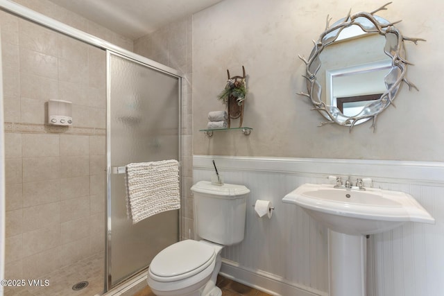 full bath with a sink, toilet, a stall shower, and wainscoting