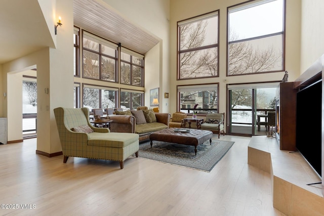 living area featuring baseboards, a high ceiling, and light wood-style flooring