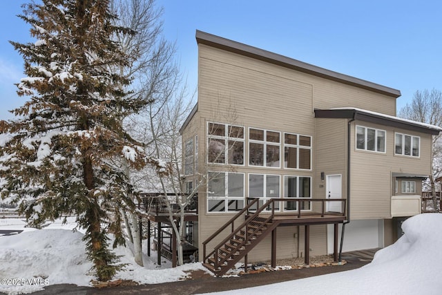 snow covered house with stairway and a wooden deck