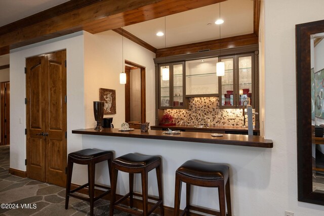 bar featuring pendant lighting, ornamental molding, tasteful backsplash, and dark colored carpet