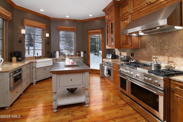 kitchen with sink, a center island, light hardwood / wood-style floors, stainless steel appliances, and wall chimney exhaust hood