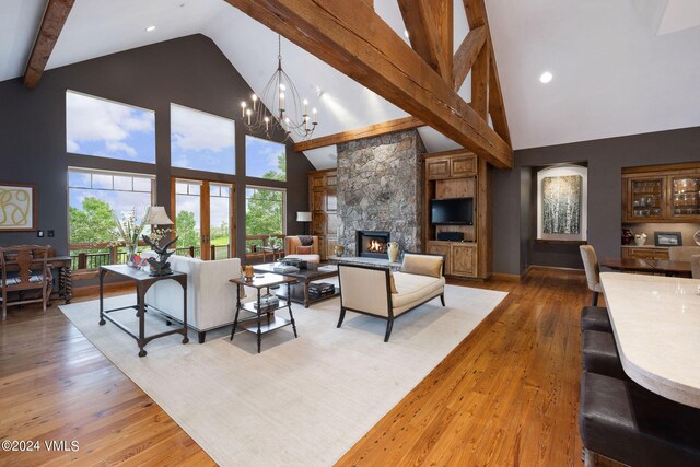 living room featuring beam ceiling, a chandelier, high vaulted ceiling, light wood-type flooring, and a fireplace