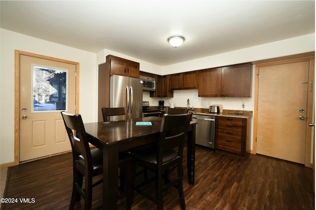 kitchen with dark brown cabinetry, appliances with stainless steel finishes, dark hardwood / wood-style floors, and dark stone countertops