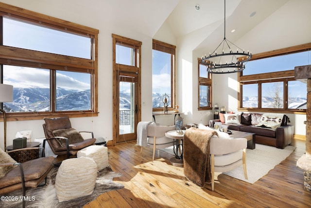 living area featuring plenty of natural light, light wood-type flooring, high vaulted ceiling, a mountain view, and a notable chandelier