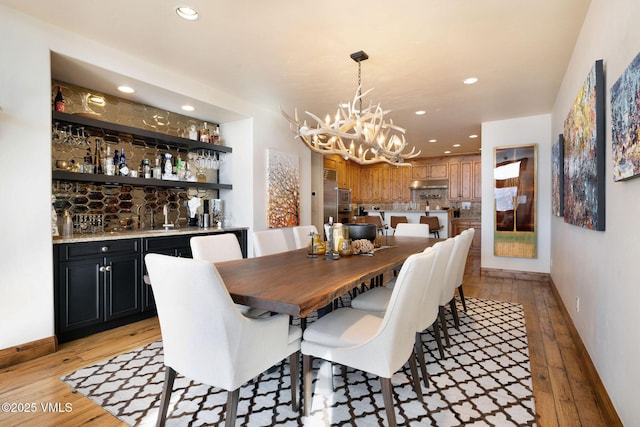 dining room with indoor wet bar, a notable chandelier, recessed lighting, light wood-style flooring, and baseboards