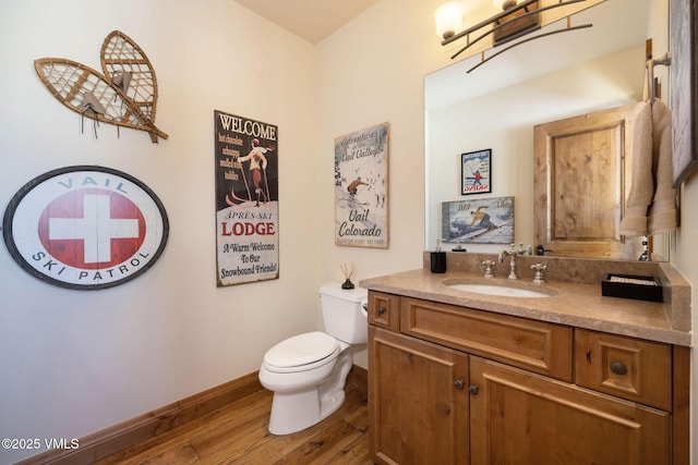 half bath with toilet, baseboards, wood finished floors, and vanity