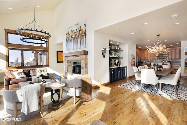 living room featuring baseboards, a towering ceiling, light wood-style flooring, a notable chandelier, and recessed lighting