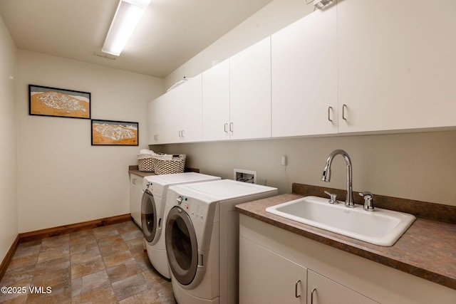 clothes washing area featuring cabinet space, baseboards, stone finish flooring, washer and dryer, and a sink