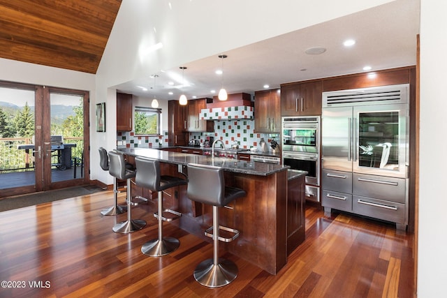 kitchen featuring a kitchen island, dark stone countertops, a breakfast bar area, hanging light fixtures, and wall chimney exhaust hood