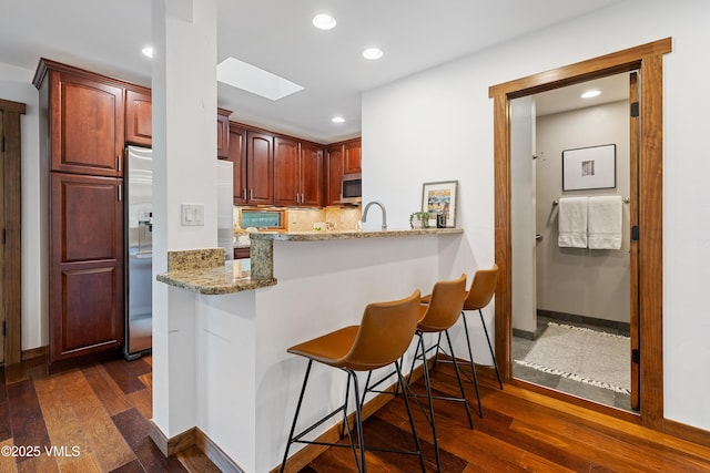 4254 Columbine Way Unit 9, Vail, CO 81657 - kitchen featuring a skylight, stainless steel microwave, a breakfast bar, light stone counters, and dark wood-style floors