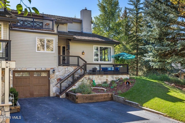 view of front of house featuring a chimney, a front lawn, an attached garage, driveway, and a balcony