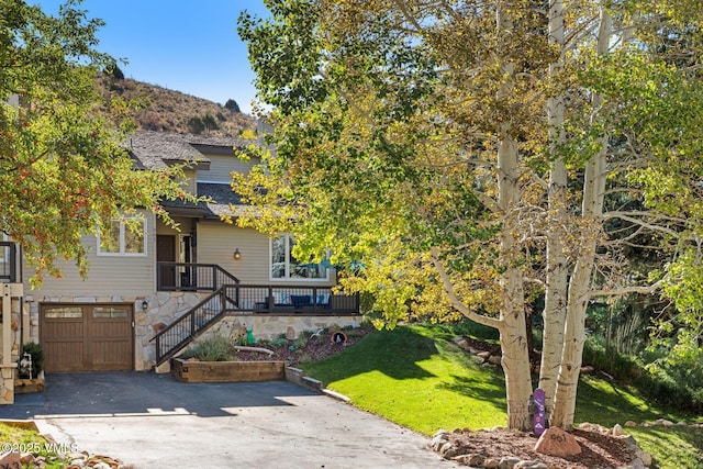 view of property hidden behind natural elements featuring asphalt driveway, a garage, a front lawn, stone siding, and a mountain view