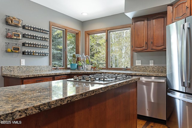 kitchen with stainless steel appliances, a sink, dark stone counters, and brown cabinets
