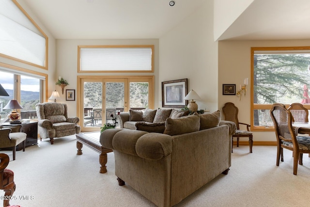 living area featuring light carpet, plenty of natural light, high vaulted ceiling, and baseboards