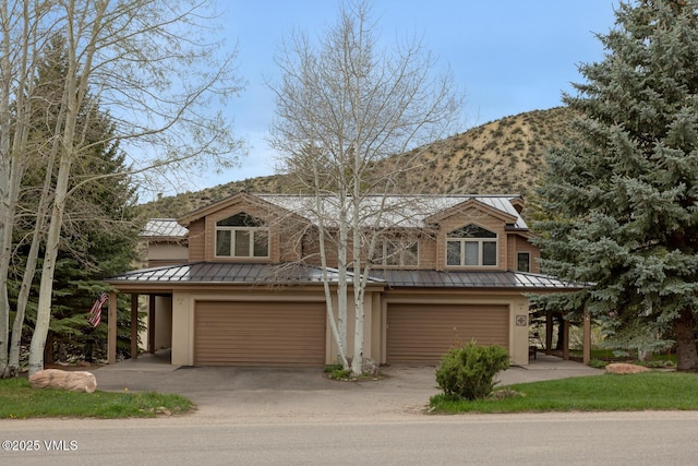 view of front facade with a standing seam roof, metal roof, a garage, driveway, and a mountain view